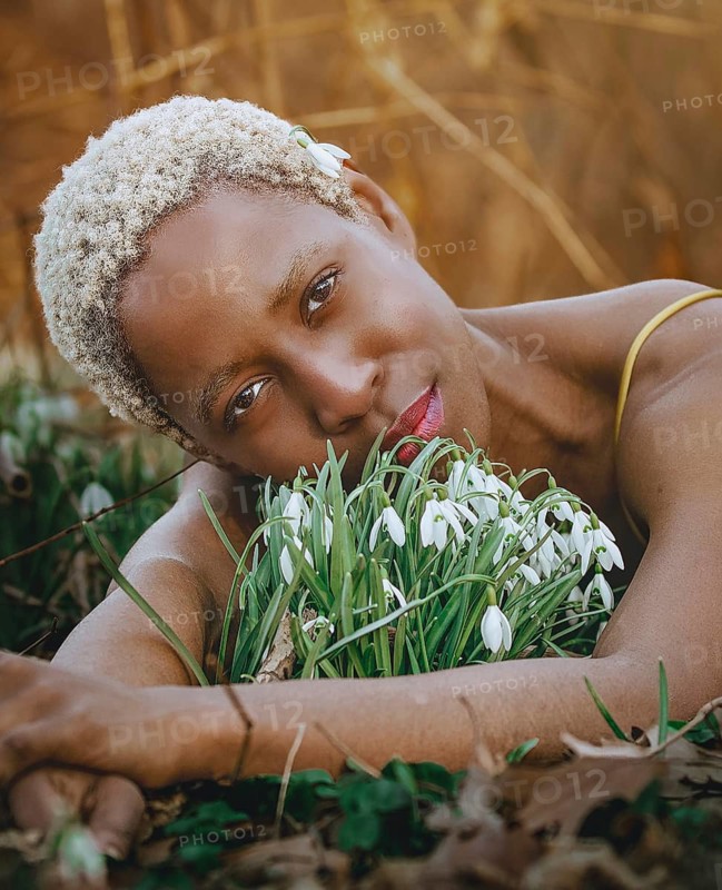 A serene moment captured as a woman rests peacefully among snowdrop flowers, embodying a deep connection with nature in Tacony Creek Park. The earthy tones enhance the calm atmosphere
