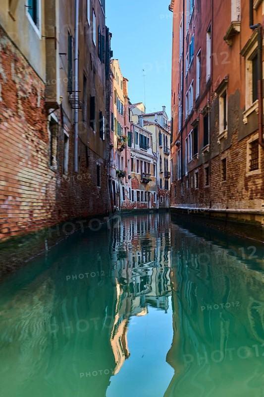 View from a gondola on a waterway in Venice going through the houses on a quiet and sunny morning in winter, Italy