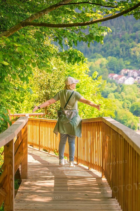 A person with outstretched arms on a wooden path with a view of a forest landscape, Panorama Holzsteg, Calw, Black Forest, Germany