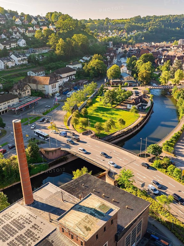 Aerial view of a bridge over a canal in a green town with surrounding houses and hilly landscape, Calw, Black Forest, Germany