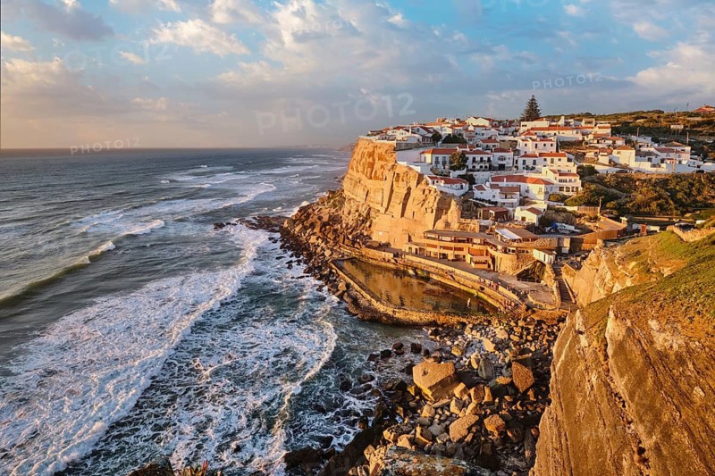 This stunning view captures the seaside village of Azenhas do Mar, perched on a cliff overlooking the Atlantic Ocean at sunset. Portugal