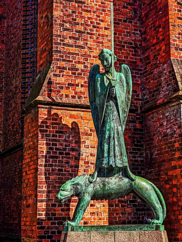 Bronze sculpture The Spiritual Warrior by the sculptor Ernst Barlach (1870 - 1938) in front of St Nicholas' Church on the Old Market Square, angel figure firmly clutching a sword, wolf-like animal, silhouette, brick outer wall, Old Town, Kiel, Schleswig-Holstein, Germany