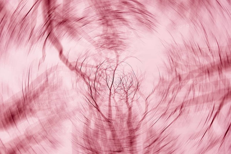 A mesmerizing abstract image with tree branches blurred into swirling patterns, creating a dynamic effect in warm pink and red tones. Perfect for creative design projects