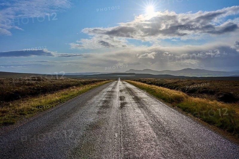 An illuminated road runs through a vast landscape under cloudy skies and strong sunlight, Tongue, Lairg, Scotland, United Kingdom, Great Britain