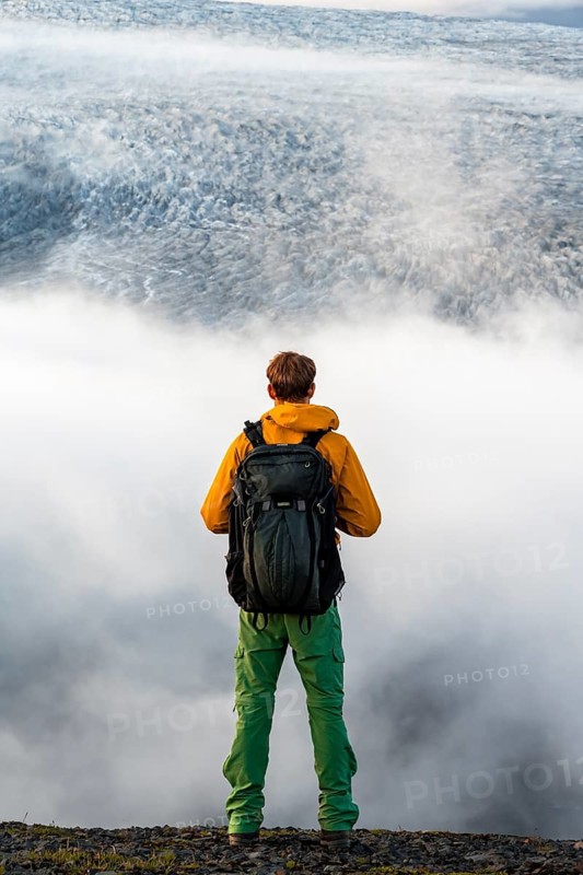 Young man in front of impressive landscape at sunset, fog, clouds moving around, glacier ice of the glacier tongue Kötlujökull, glacier Myrdalsjökull, Pakgil, Iceland