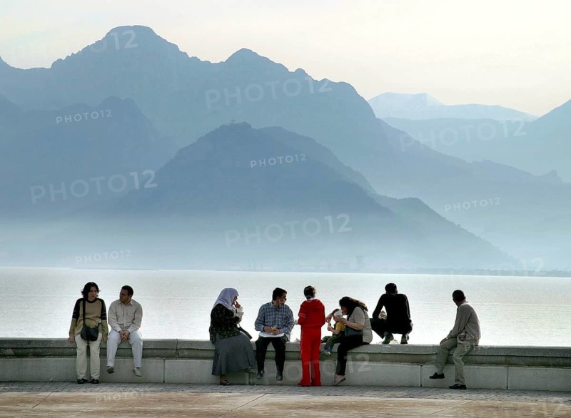 Antalya, TUR, 10.04.2004 - Turks sit on a wall on the waterfront in Antalya, Turkey. In the background the Taurus Mountains, Turkey