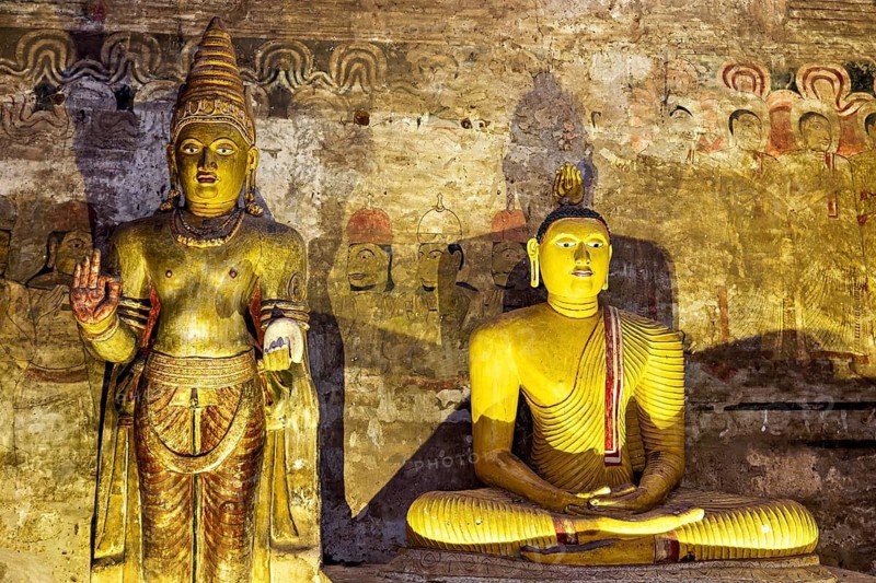 Two Buddha statues, partly in shade, in front of a painted wall, The cave temple of Dambulla in Sri Lanka