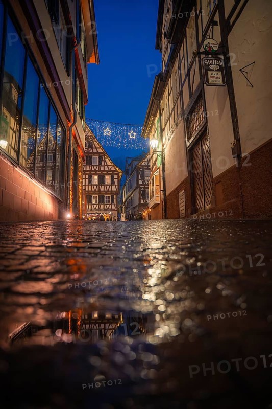 Wet cobblestone alley in historic old town illuminated with Christmas lights, romantic and dreamy, Christmas market Calw, Black Forest, Germany