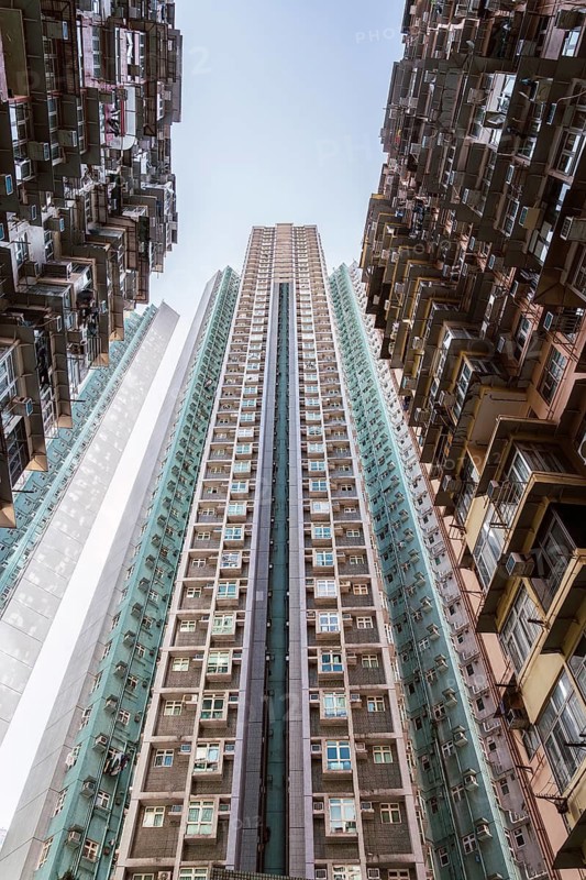 Low angle of towering residential buildings soar, showcasing Hong Kong's dense urban architecture. This upward perspective highlights the city's unique structural design and overpopulation challenges