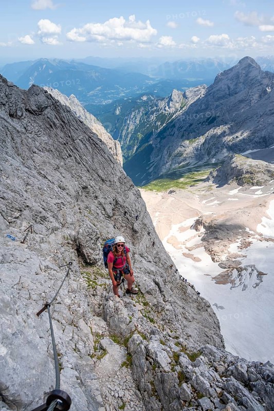Mountaineer with helmet climbing in a secured via ferrata, Zugspitz via ferrata, ascent to the Zugspitze, view of mountain basin with snowfield of the Höllentalferner and Höllental, Wetterstein range, Wetterstein range, Bavaria, Germany