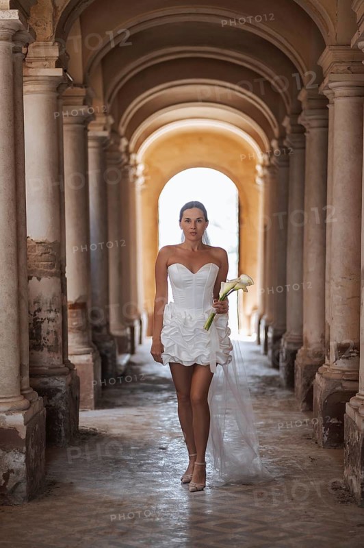 A bride walks elegantly through the ancient arches of a historic villa in Treia, Macerata. Her white dress and bouquet contrast with the villa's classical architecture