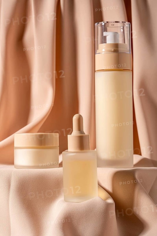 Skincare products elegantly arranged on soft peach curtain Includes dropper bottle, jar, and pump bottle, creating a luxurious aesthetic perfect for beauty concepts