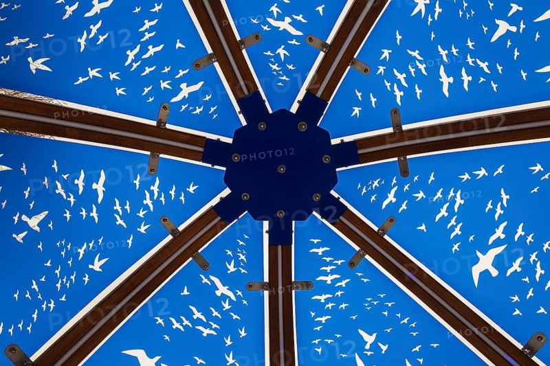 Close-up of backlit blue tinted plexiglass and curved wood panels canopy decorated with white flock of birds in flight theme motifs inside interactive cocoon rocking chair created by Olivier Landreville, Horizon Art Installation, Ile des Moulins, Old Terrebonne, Quebec, Canada