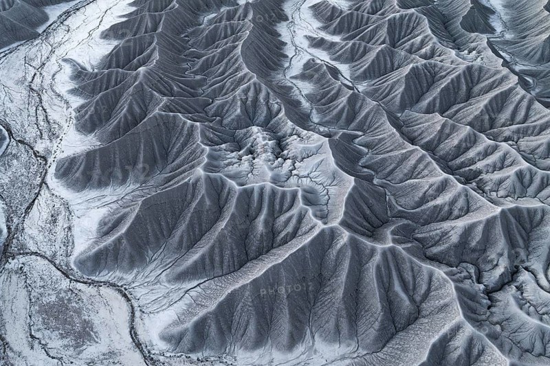 Stark aerial perspective of Caineville Mesa near Hanksville, Utah, coated in snow, highlighting the sculpted terrain and erosion patterns