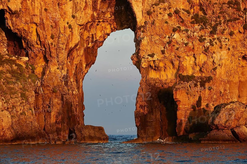 Detail of a rock arch at sunrise with birds in the sky, morning light, Tsichli Babas islet, Navarino Bay, Pylos, Peloponnese, Greece
