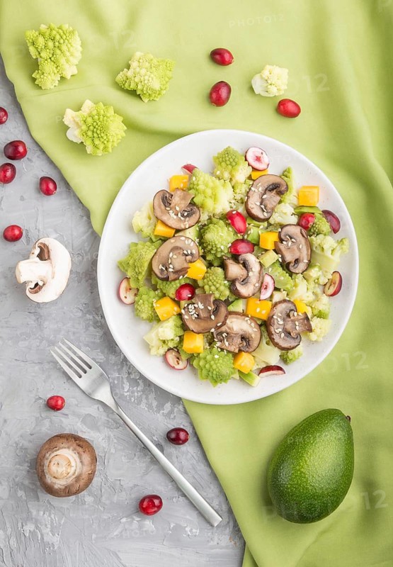 Vegetarian salad from romanesco cabbage, champignons, cranberry, avocado and pumpkin on a gray concrete background and green textile. top view, flat lay, close up