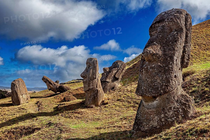Several moai in a grassy hilly landscape under a partly cloudy sky on Easter Island, The moai statues on Easter Island in the Pacific Ocean