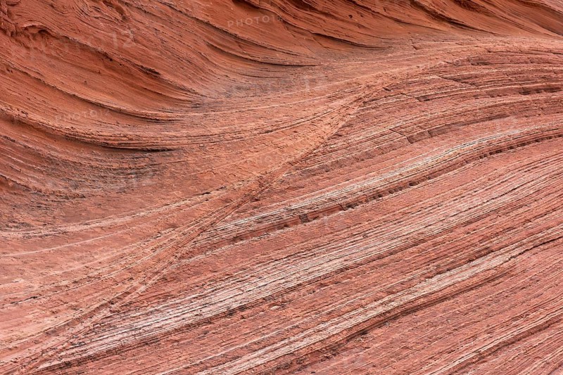 Red sandstone formations create a visually striking abstract texture with layered patterns. The natural curves and lines evoke the beauty of geological formations