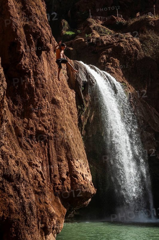 OUZOUD, MOROCCO - OCTOBER 5, 2024: A Moroccan young boy jumps from the high rock into the water under a waterfall Ouzoud