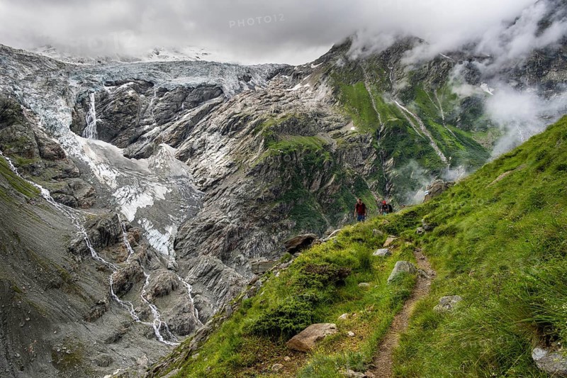 Two mountaineers on a hiking trail, cloudy mountain landscape with Grindelwald-Fiescherfirn glacier, Bernese Alps, Bernese Oberland, Switzerland