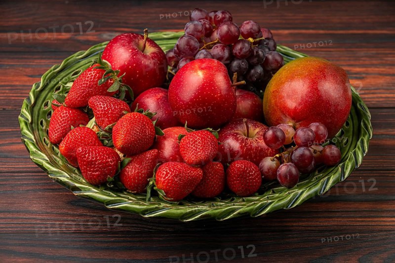 Strawberries, apples, grapes and mango in a green bowl on wood