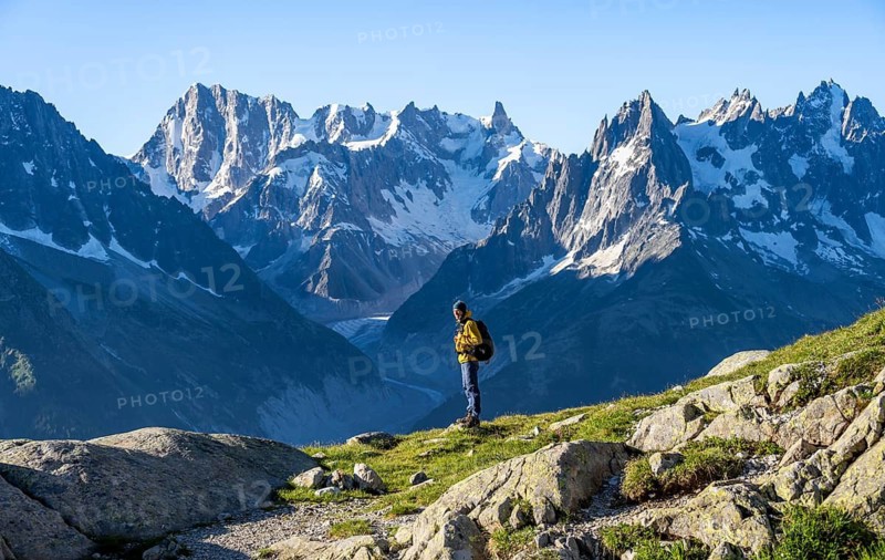 Young man in front of impressive mountain landscape in morning light, picturesque mountain landscape with imposing mountain peaks and glaciers, Mer de Glace glacier, Grandes Jorasses in the background, Mont Blanc Massif, Chamonix-Mont-Blanc, Haute-Savoie, France