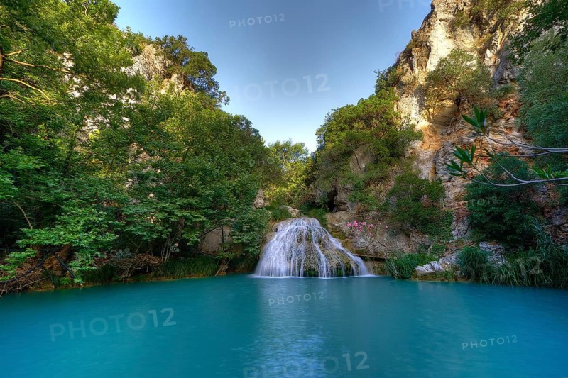 A waterfall plunges into a large turquoise-blue pool surrounded by green foliage and rocks, waterfalls, ponds, Polylimnio, Peloponnese, Greece