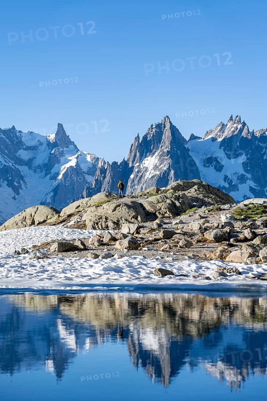 Young man in front of impressive mountain landscape in morning light, reflection in the Lac Blanc mountain lake, mountain summit, Aiguille Verte, Grandes Jorasses, Aiguille du Moine, Mont Blanc, Mont Blanc Massif, Chamonix-Mont-Blanc, Haute-Savoie, France