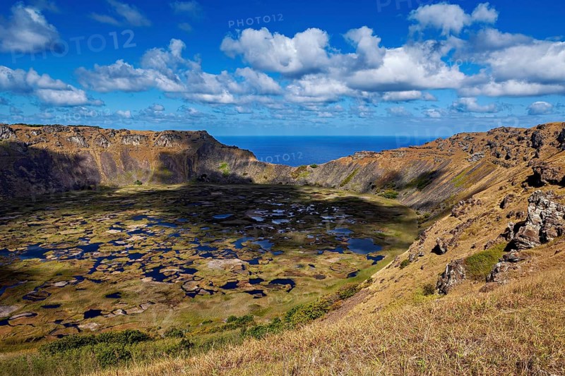 Crater with deep shadows and sweeping views over rocky landscapes to blue skies, the Ranu Kau volcano on Easter Island in the Pacific Ocean