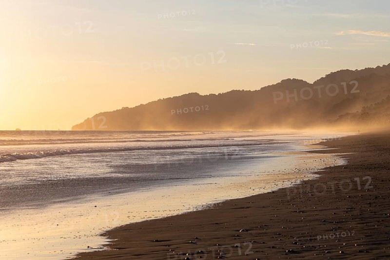 The low sun's golden light illuminates the ocean spray on Carate Beach, with views of Corcovado NP at sunset. Costa Rica