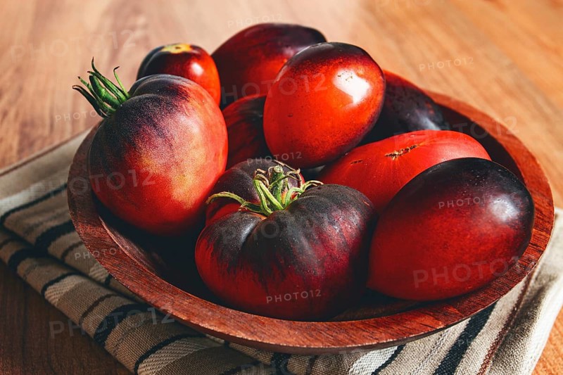 Freshly picked tomatoes, of the Black Beauty variety, in a wooden bowl, close-up, on the kitchen table
