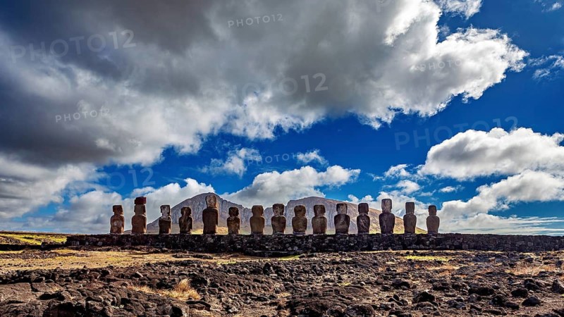 Moai statues stand under a sky with dramatic clouds on a rocky surface, The Moai statues on Easter Island in the Pacific Ocean