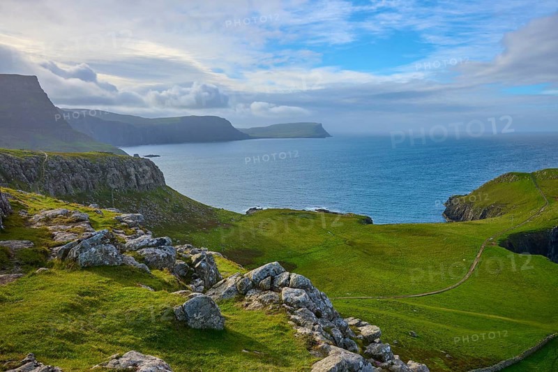 Rocky coast with green hills under a cloudy blue sky, Waterstein Head, Waterstein, Isle of Skye, Scotland, United Kingdom, United Kingdom