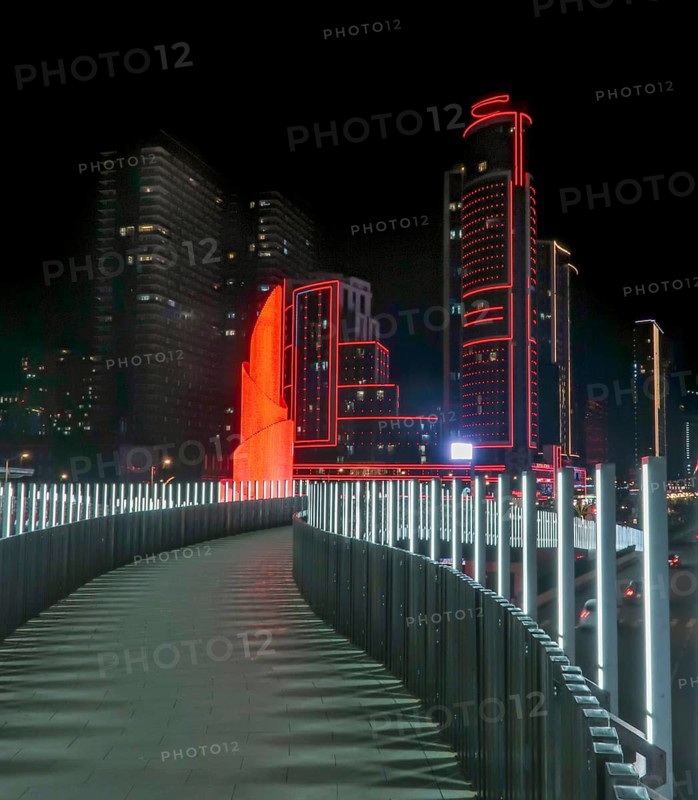 Night view of a modern cityscape in Georgia, featuring a brightly illuminated skyscraper adorned with red lights. A futuristic walkway with glowing rails leads the scene