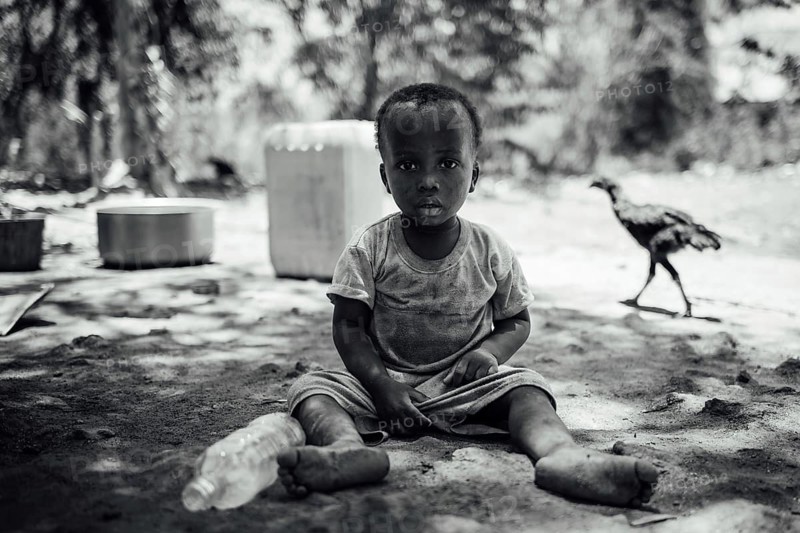 MICHAMVI KAE, ZANZIBAR - OCTOBER 17, 2025: A monochrome portrait of a young child sitting on the ground outdoors, featuring a chicken in the background and a natural, candid atmosphere, african, ethnic, ethnicity, africa