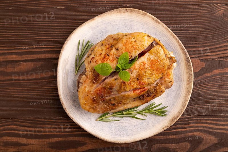 Fried Turkey Thigh with spices and rosemary on plate on brown wooden background. top view, flat lay, close up
