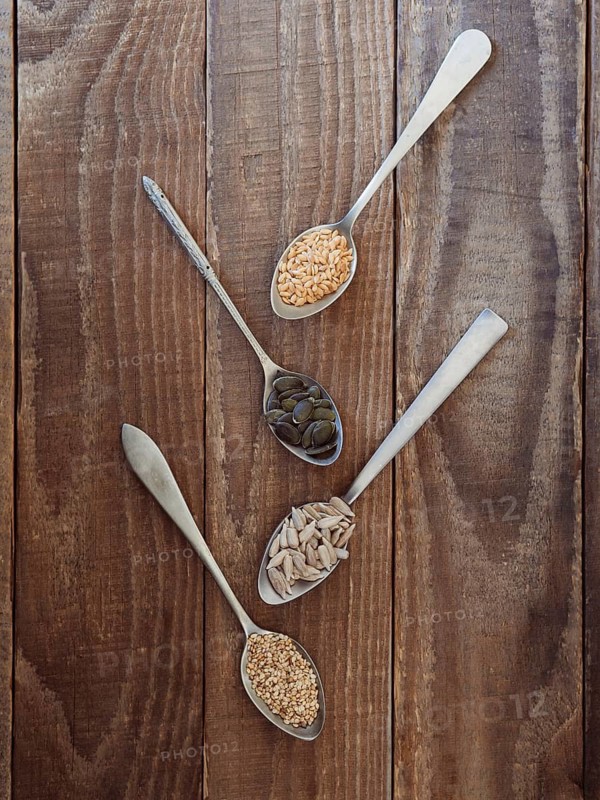 Spoons holding flax, pumpkin, sunflower, and sesame seeds on rustic wood background