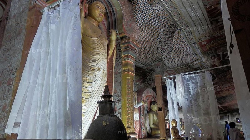 Cave room with large Buddha statue, artfully painted walls and curtains, Dambulla cave temple, Sri Lanka