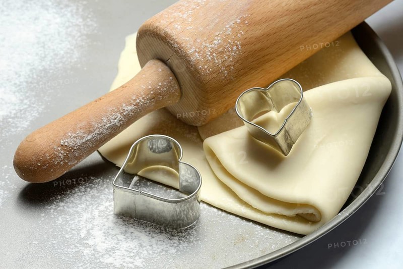 Rolled dough on cake tray with dough rollers and cookie cutters