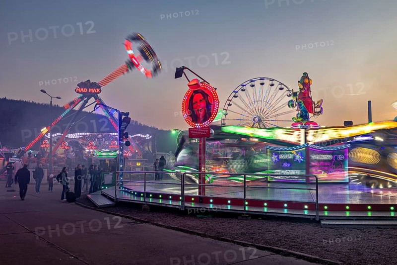 Lively fair with illuminated rides in motion at dusk, carousel and the hustle and bustle of summer winnings in Eisenach
