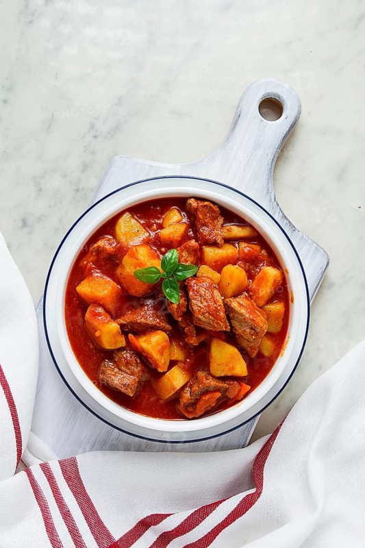 Potatoes stewed with meat, in tomato sauce, with spices and herbs, no people, on a white table