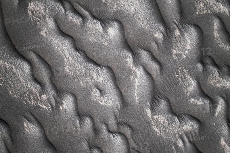 Close-up image capturing the intricate patterns formed on a black sand beach, showcasing textures and slight discolorations
