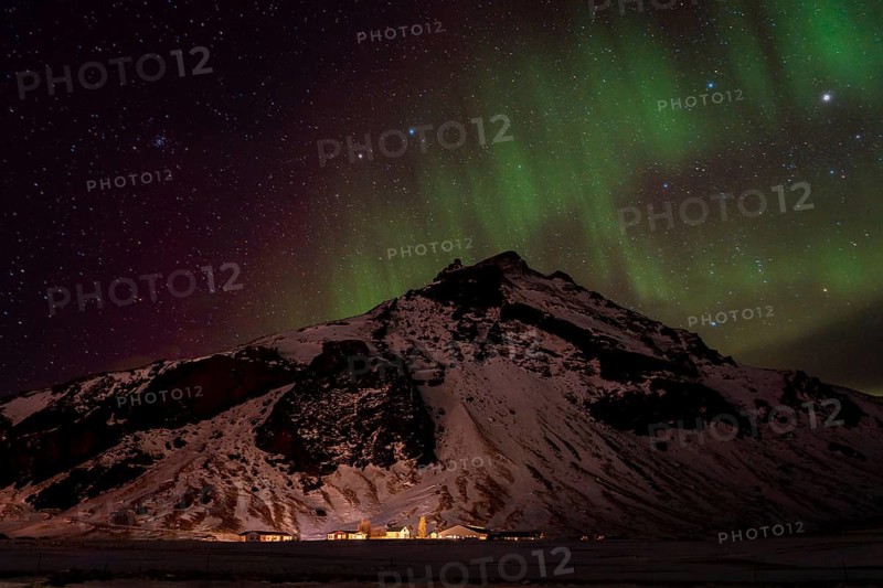 A breathtaking view of the Northern Lights dancing over a snow-covered mountain in Iceland. The vibrant aurora and clear starry night sky create a stunning winter scene