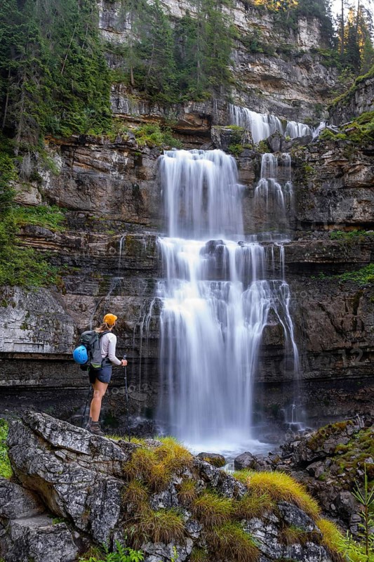 Young pretty hiker standing on rocks in front of Cascata di Mezzo waterfall, long exposure, Vallesinella, Brenta, Trentino, Italy