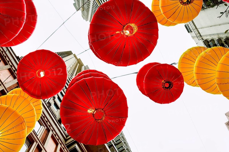 From below vibrant red and yellow lanterns hanging between buildings in Hong Kong during the celebration of Chinese New Year, showcasing traditional festive decorations against a urban backdrop