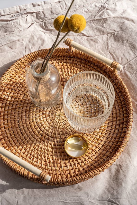 From above vitamin supplements, including Omega 3 fish oil capsules and Vitamin D3, neatly placed on a rattan tray beside a glass of water, under soft natural light