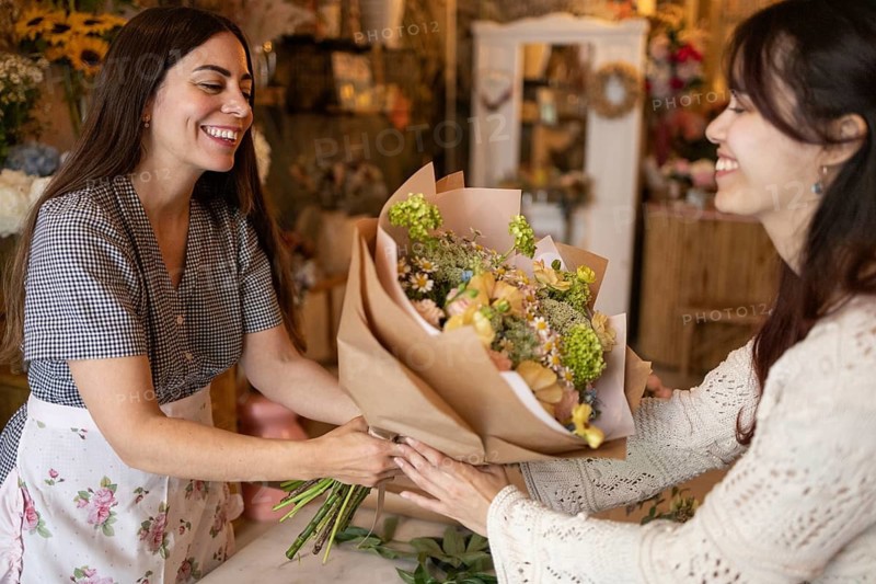 A woman joyfully present a floral bouquet in their vibrant florist shop, surrounded by beautiful blooms and natural decor, embodying creativity