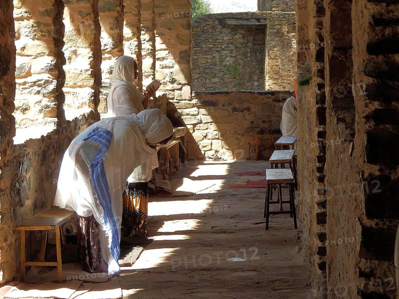 People pray in a shady area of stone corridor architecture, Debre Birhan Selassie Church, Fasil Ghebbi, Historic Stone Building, Orthodox Church, Gondar, Ethiopia
