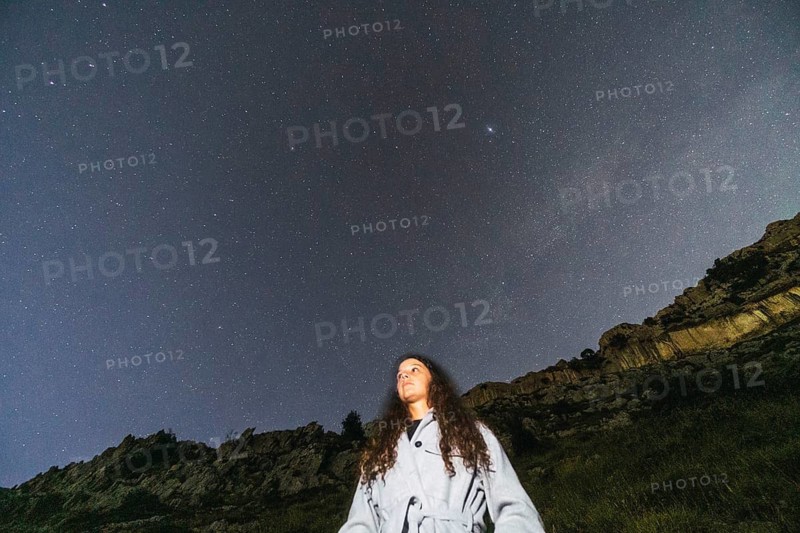 A person stands under a star-filled night sky, surrounded by nature's tranquility A drone captures the celestial spectacle, emphasizing the vast beauty of the universe