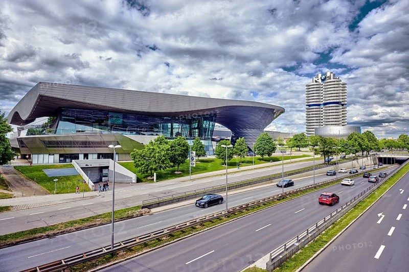 BMW Welt, commercial building, modern architecture, road, lanes, guardrail, central strip, lantern, cars, meadow, trees, elevated perspective, cloudy, cumulus clouds, Georg-Brauchle-Ring, Munich, state capital, district-free city, Bavaria, Germany